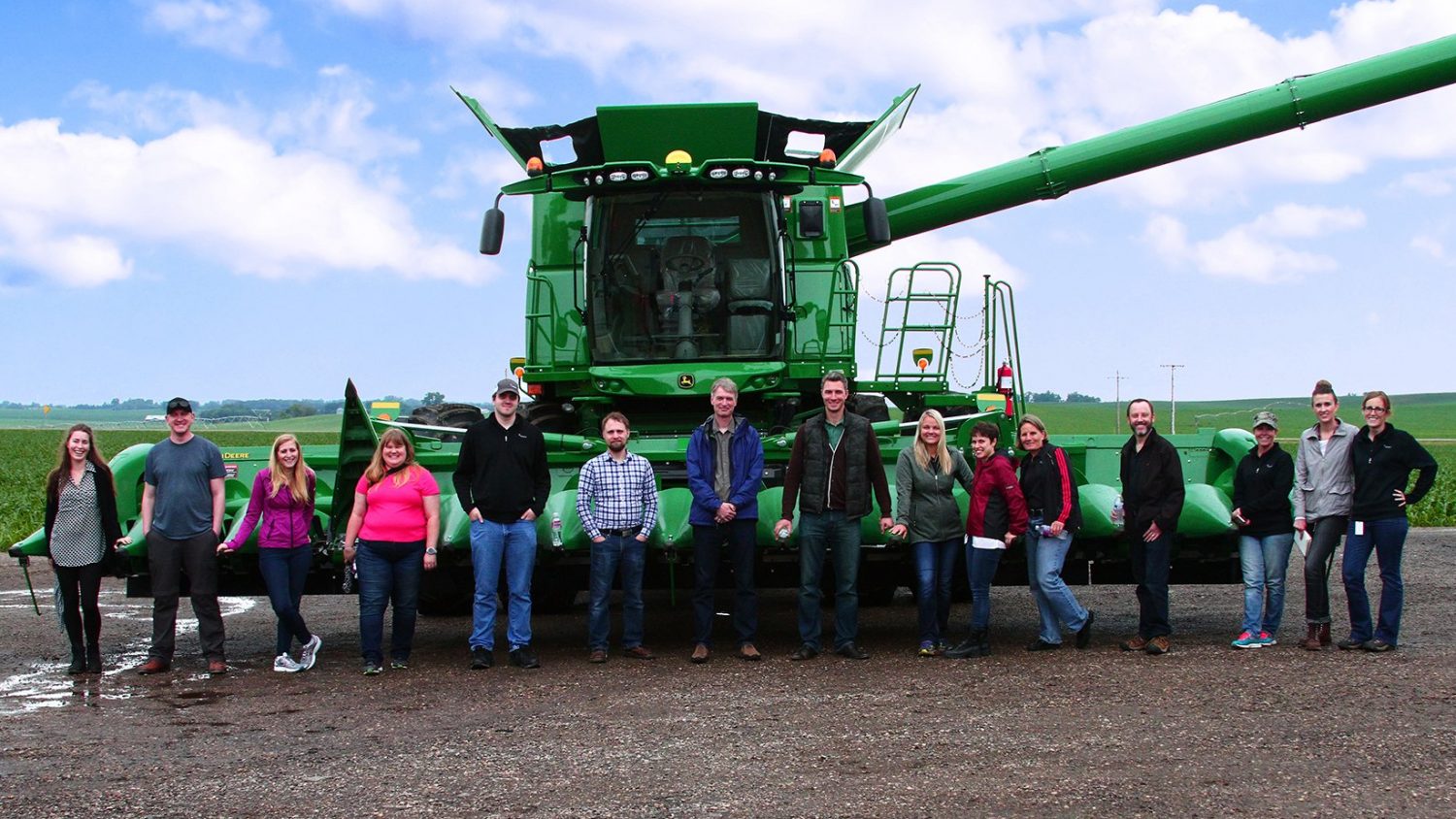 A group of people standing on a farm in front of a combine