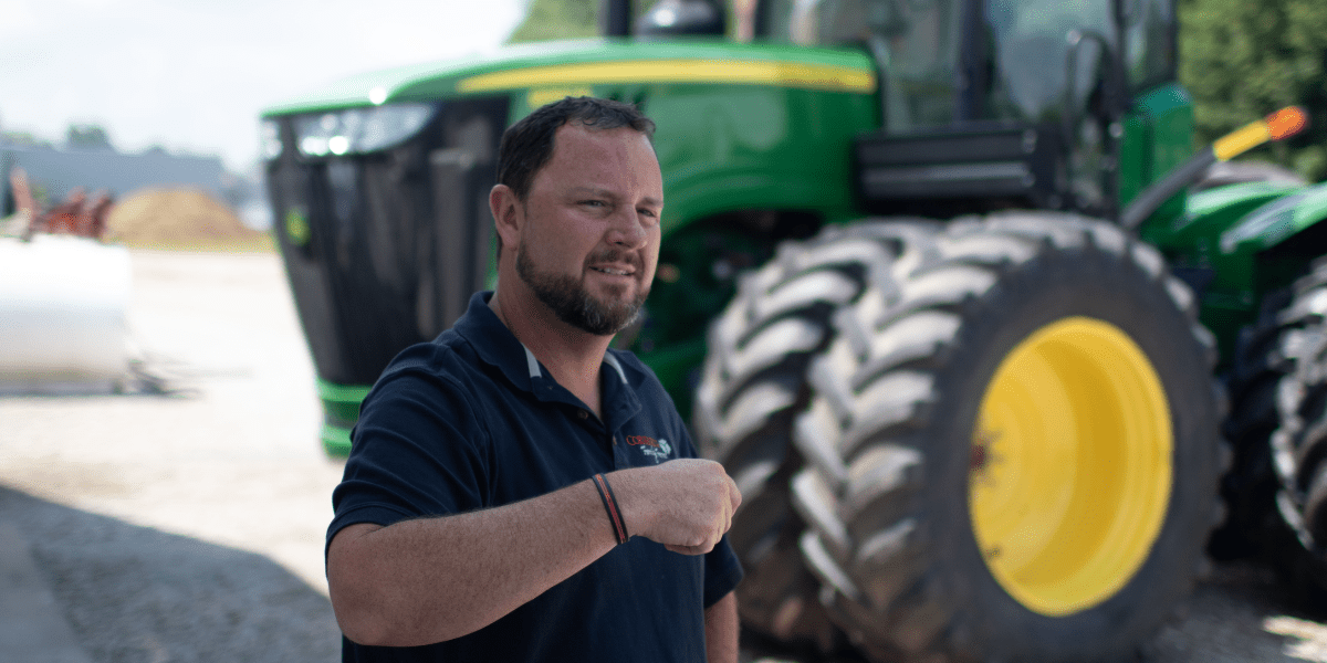 Pensive farmer stands before a John Deere tractor near a field