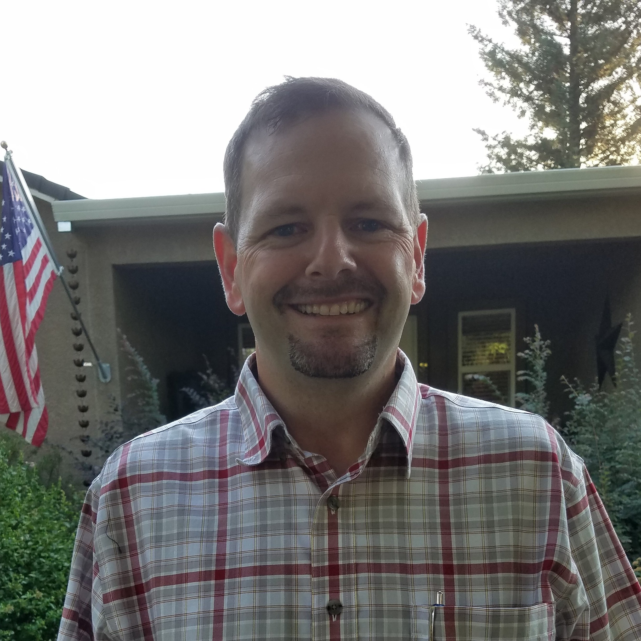 headshot of Pat Andersen standing in front of building with American flag in backgroun